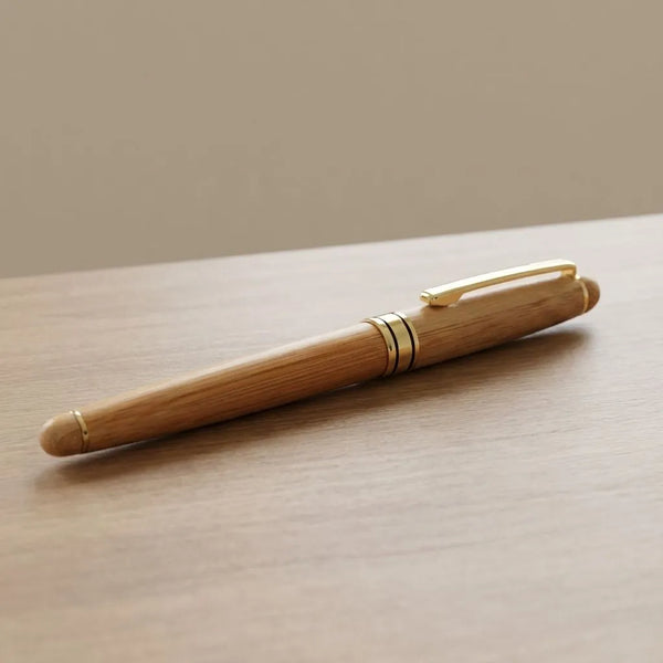 Bamboo Roller Pen placed on a wooden surface showcasing its elegant design and golden accents.