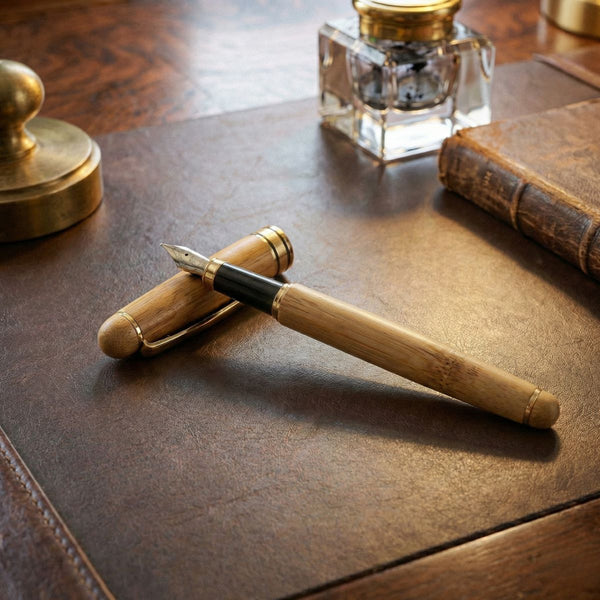 Premium Bamboo Pen on a leather desk with an ink bottle and a book.