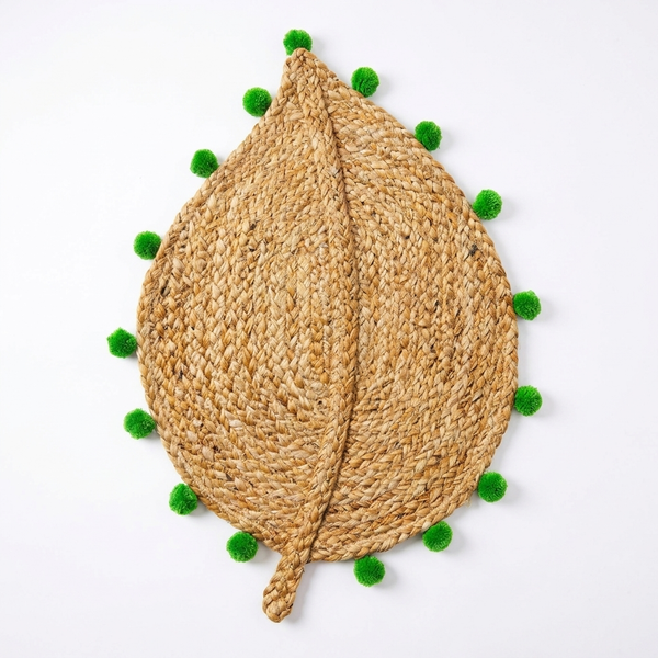 Leaf Jute Weave Mat, Sage colourway — leaf-shaped jute mat with green pompom trim, top-down on a plain background.
